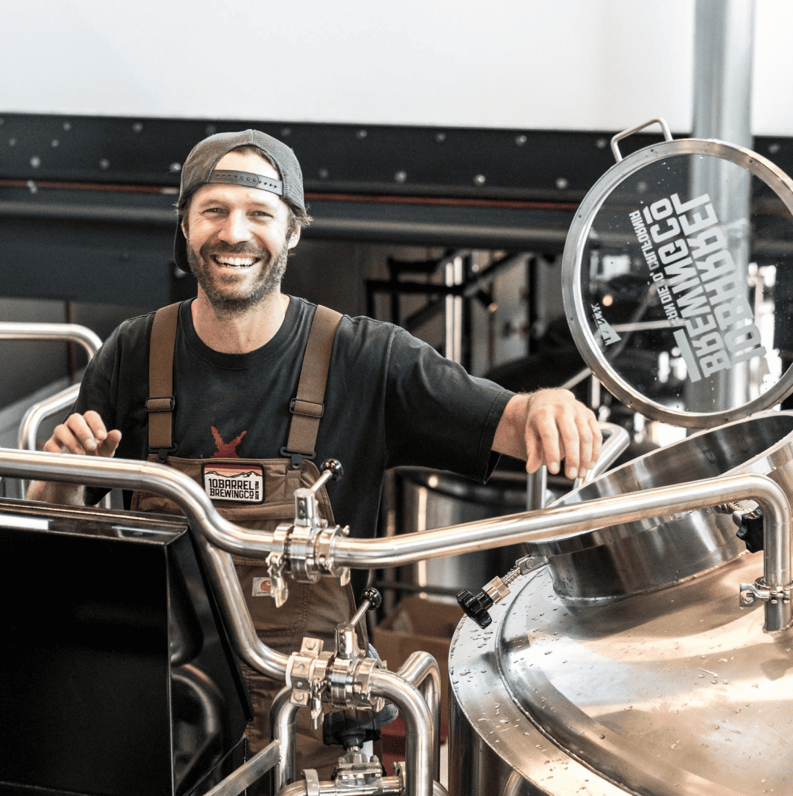 A smiling man in his workshop standing next to brewing equipment