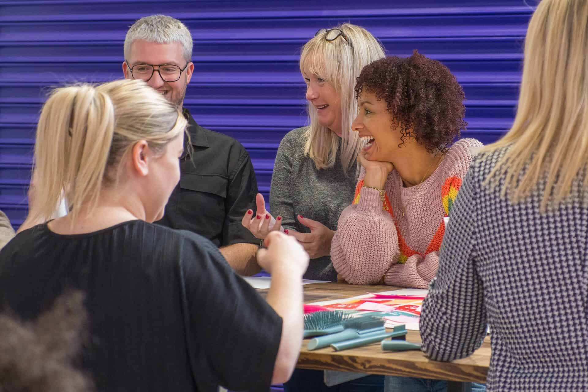 People standing around a table in light industrial spaces, smiling and laughing while working.