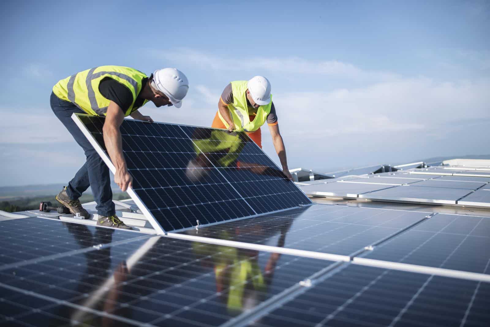 A team of two sustainability engineers installing solar panels on a roof.